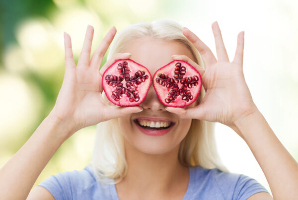 Eine Frau hält sich je einen aufgeschnittenen Granatapfel vor die Augen und lächelt