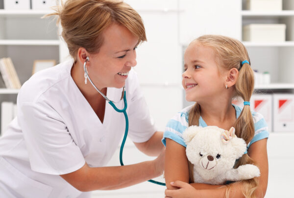 Kleines Mädchen mit Kuscheltier im Arm wird von einer Arzthelferin untersucht