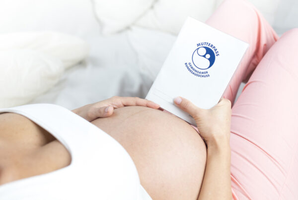 Frau mit Schwangerschaftsbauch und einem Mutterpass in der Hand