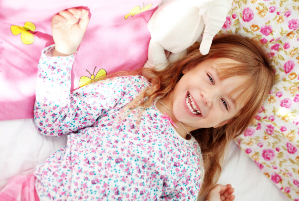 Ein Kind im Schlafanzug liegt lächelnd mit einem Kuscheltier im Bett.