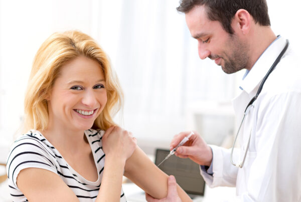 Eine Frau lächelt in die Kamera, während sie eine Spritze mit einer Impfung von einem Arzt bekommt.