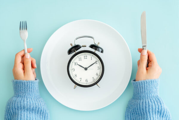 Zwei Hände mit Messer und Gabel neben einem Teller auf dem Tisch, auf dem eine Uhr abgebildet ist.